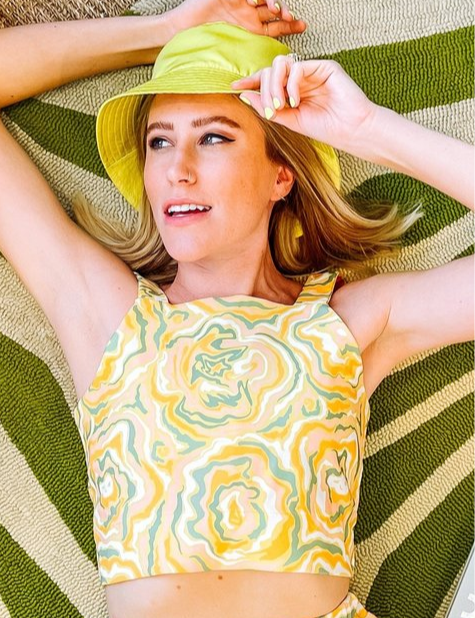 A woman wearing a yellow crop top with a green and orange abstract print on it