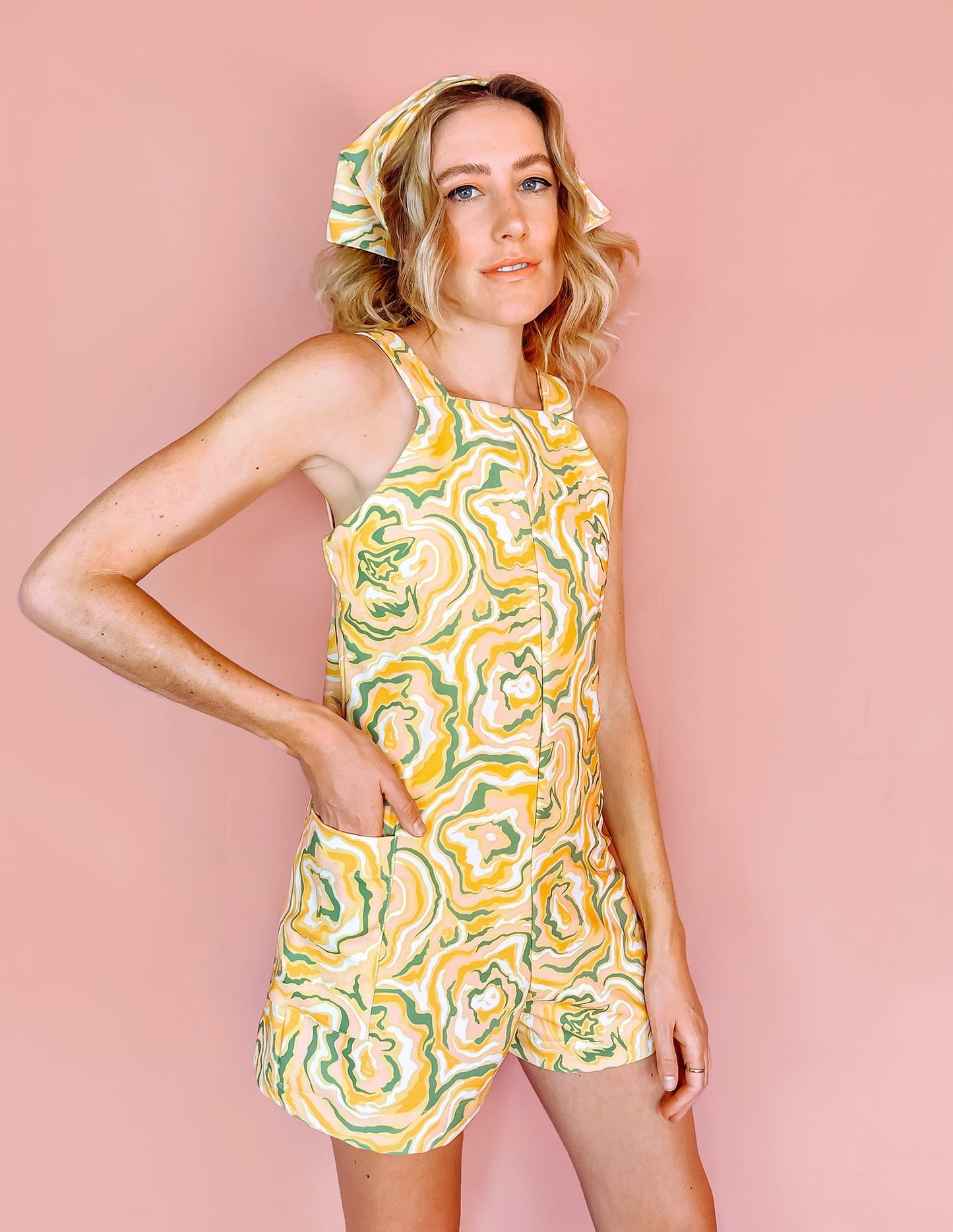 A woman wearing a yellow romper with green orange and white swirls on