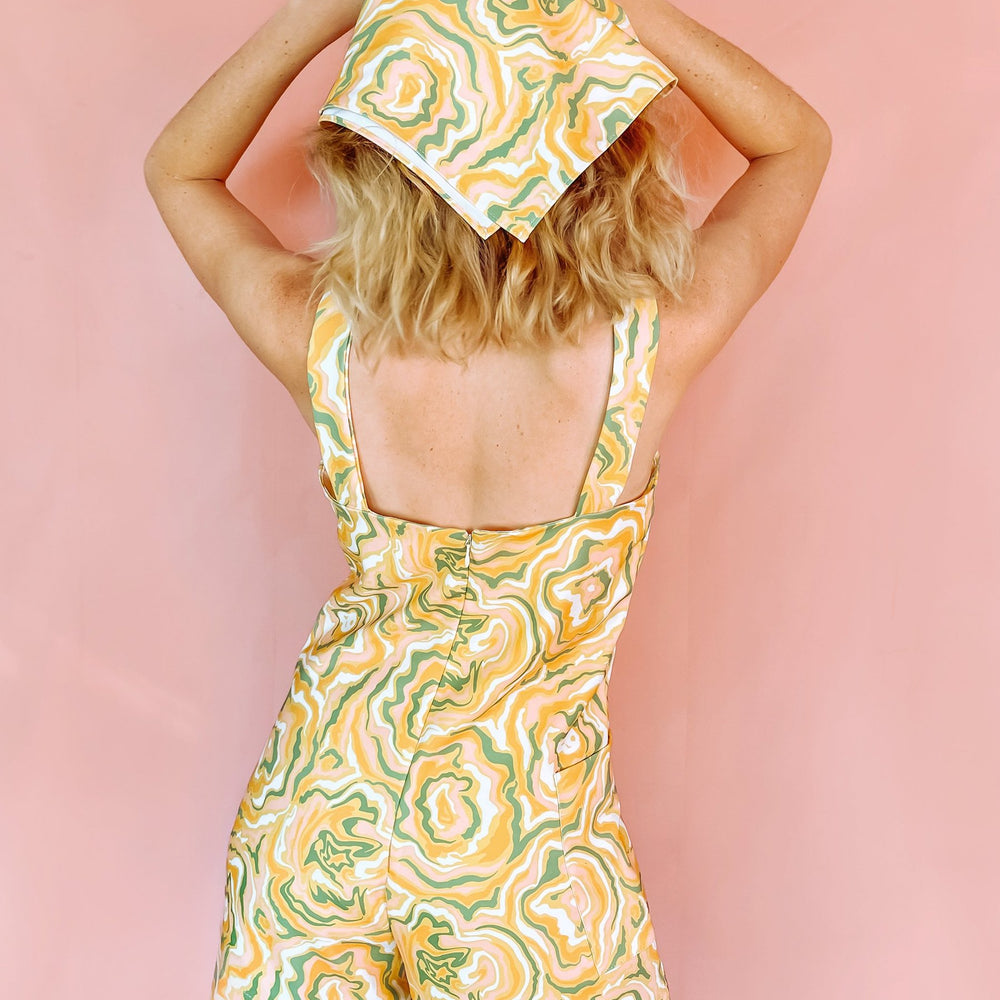 
                      
                        A woman wearing a yellow romper with green orange and white swirls on
                      
                    