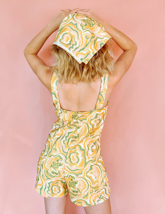 A woman wearing a yellow romper with green orange and white swirls on
