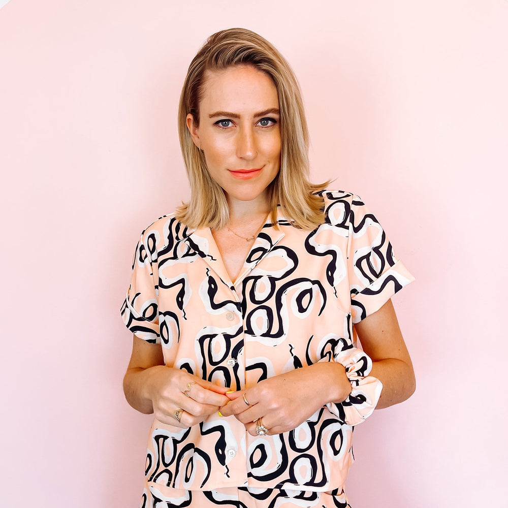 
                      
                        A woman wearing a pink shirt with a black abstract print on it
                      
                    