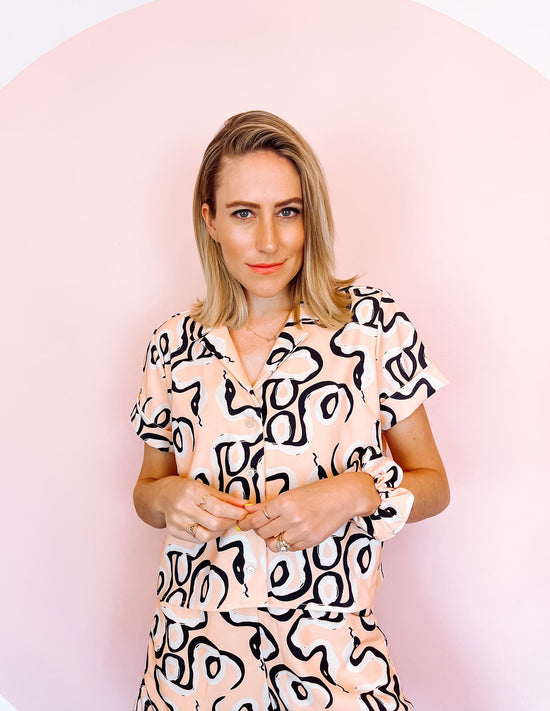 A woman wearing a pink shirt with a black abstract print on it