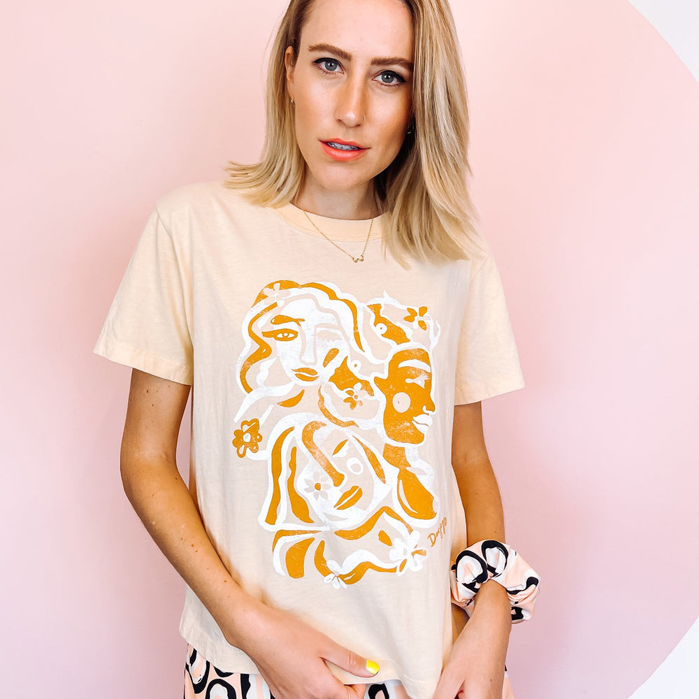 
                      
                        A woman wearing white t-shirt with an orange and white abstract print on, in the shape of faces.
                      
                    