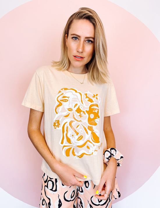 A woman wearing white t-shirt with an orange and white abstract print on, in the shape of faces.