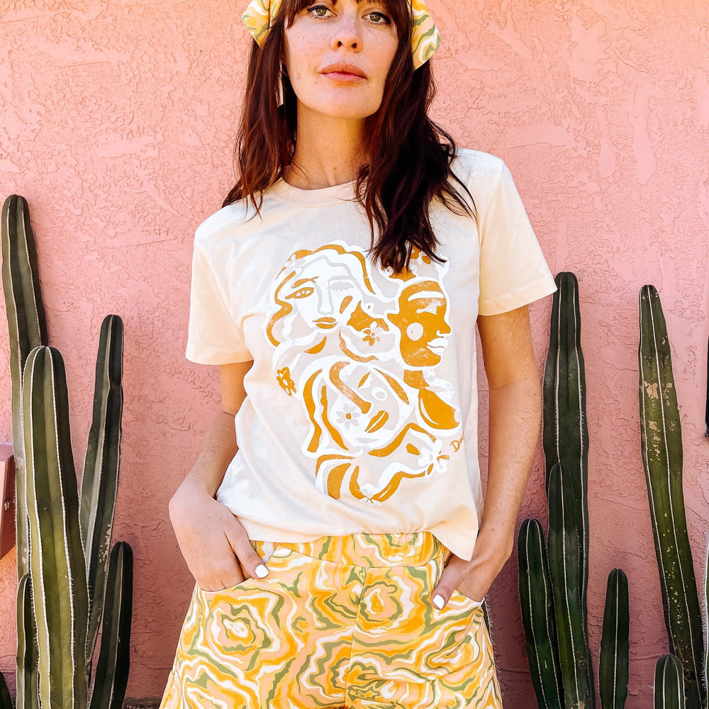 
                      
                        A woman wearing white t-shirt with an orange and white abstract print on, in the shape of faces.
                      
                    