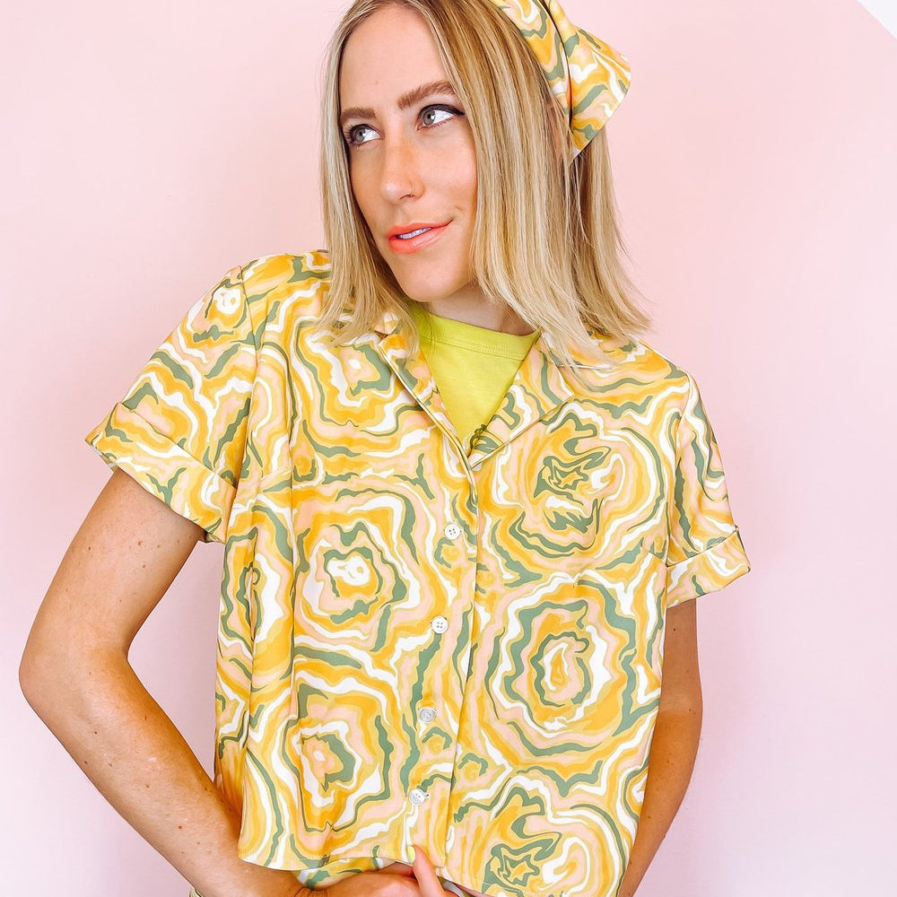 
                      
                        A woman wearing a yellow short sleeve shirt with a green and orange abstract print on it.
                      
                    