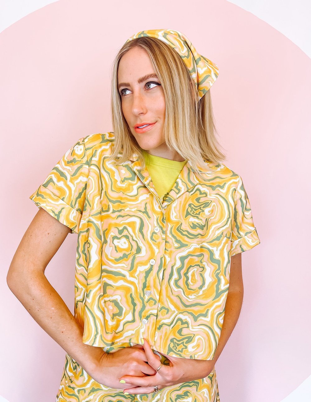A woman wearing a yellow short sleeve shirt with a green and orange abstract print on it.